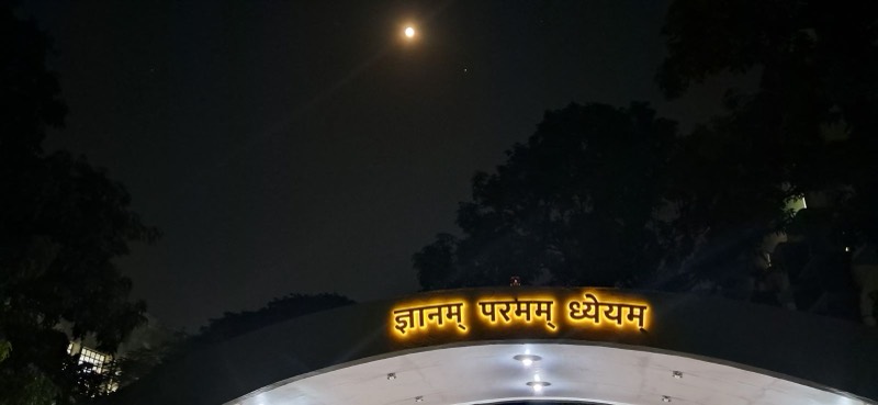 The moon over an illuminated Sanskrit sign at night